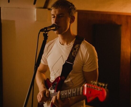 Irish Indie-pop artist Fintan McKahey plays the guitar singing into the mic
