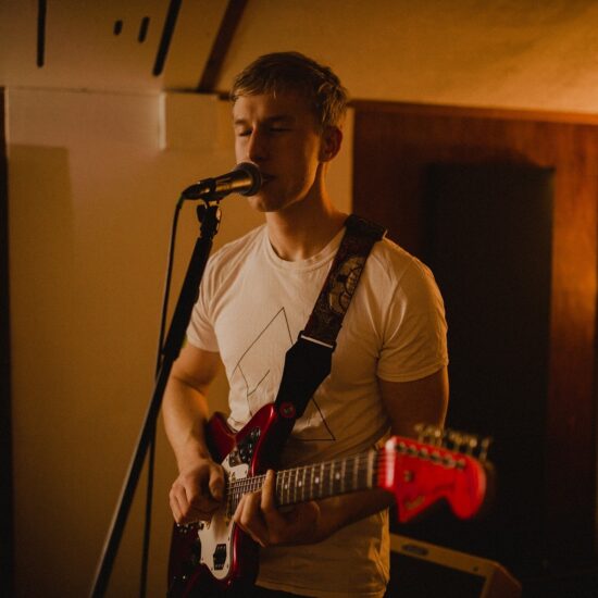 Irish Indie-pop artist Fintan McKahey plays the guitar singing into the mic